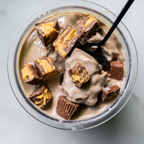 A bowl of dairy-free ice cream with chunks of chocolate peanut butter cups and chocolate pieces, with a spoon inserted into the ice cream.