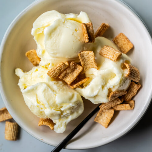 A bowl of Banana Protein Ice Cream topped with cereal pieces, with a spoon placed inside. Perfect for a low carb treat made effortlessly with the Ninja Creami.