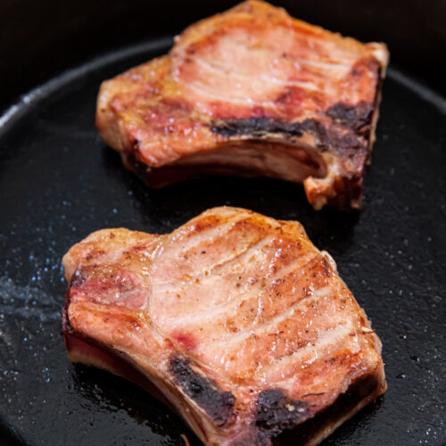 Two juicy Traeger pork chops are sizzling in a black cast iron pan.