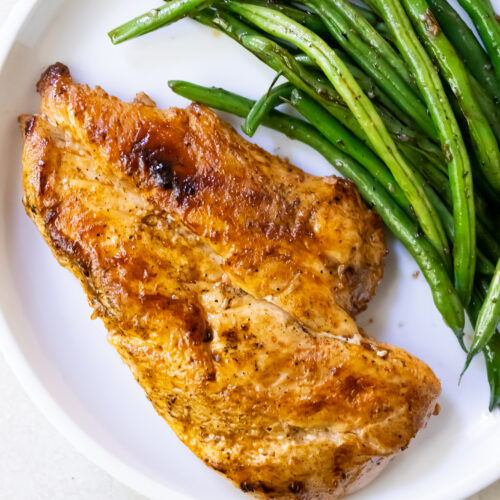 A white plate with a serving of succulent roasted chicken breast and crisp green beans, perfectly cooked on a Blackstone griddle.