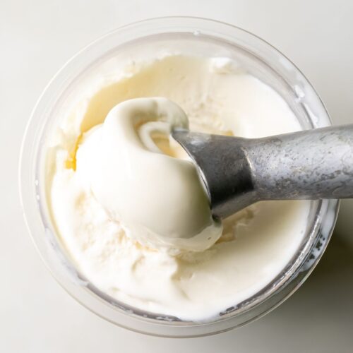 A metal spoon scoops a portion of protein ice cream from a clear container, perfectly prepared by the Ninja Creami.