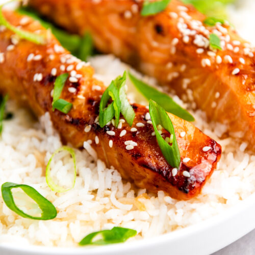 Try our teriyaki salmon recipe, featuring grilled salmon with sesame seeds and green onions. It's perfectly served on a bed of rice with asparagus on the side for a delightful meal.