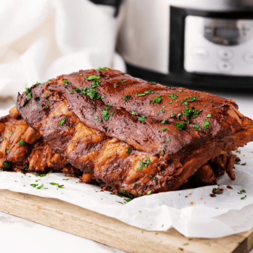 Cooked slab of soy spareribs garnished with chopped parsley on parchment paper, with a slow cooker in the background.