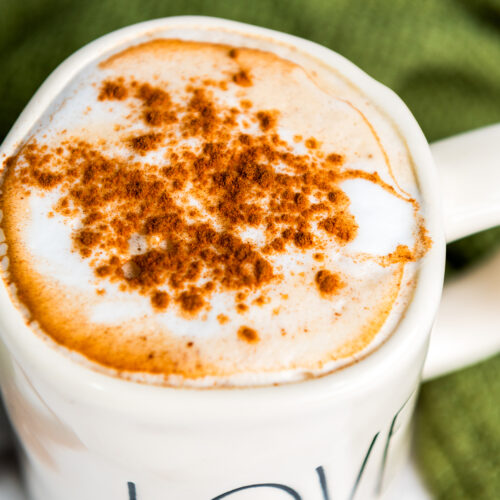 A mug of frothy latte topped with cinnamon, nestled beside a green cloth.