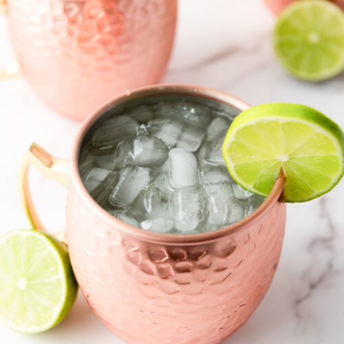 Copper mugs filled with ice-cold Moscow Mules, each garnished with a lime slice, are arranged on a marble surface, creating the perfect display for this classic recipe.
