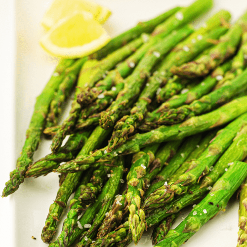 A plate of perfectly roasted asparagus spears, prepared using an air fryer, garnished with sea salt and accompanied by fresh lemon wedges.