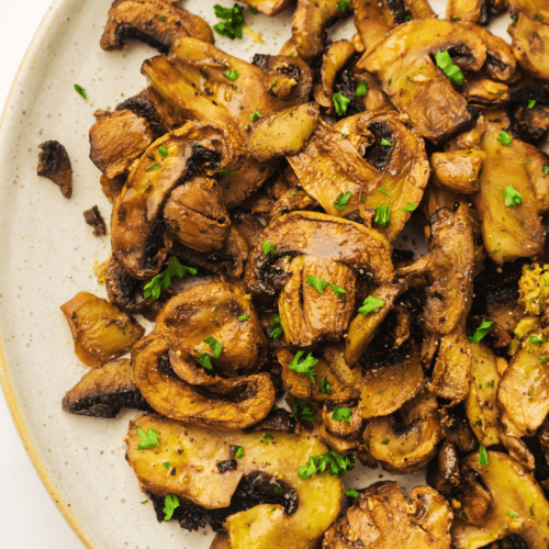 A plate of air fryer garlic mushrooms garnished with chopped parsley.
