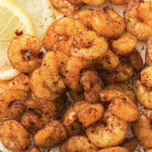 Close-up of perfectly spiced, air fryer shrimp garnished with fresh herbs and lemon slices on the side.