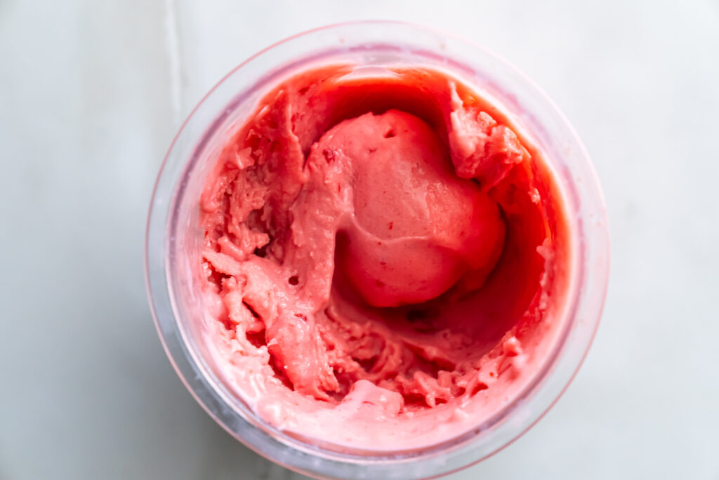 A container of pink ice cream with a smooth, creamy texture and a partially scooped ball visible.