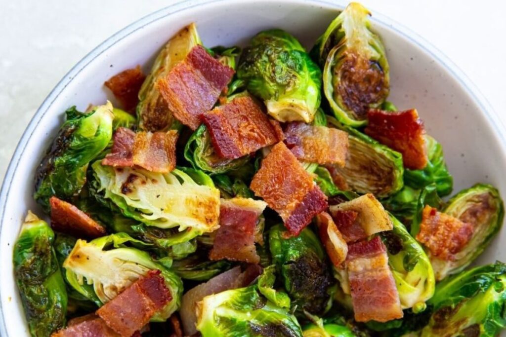 A bowl of roasted Brussels sprouts topped with crispy bacon pieces.