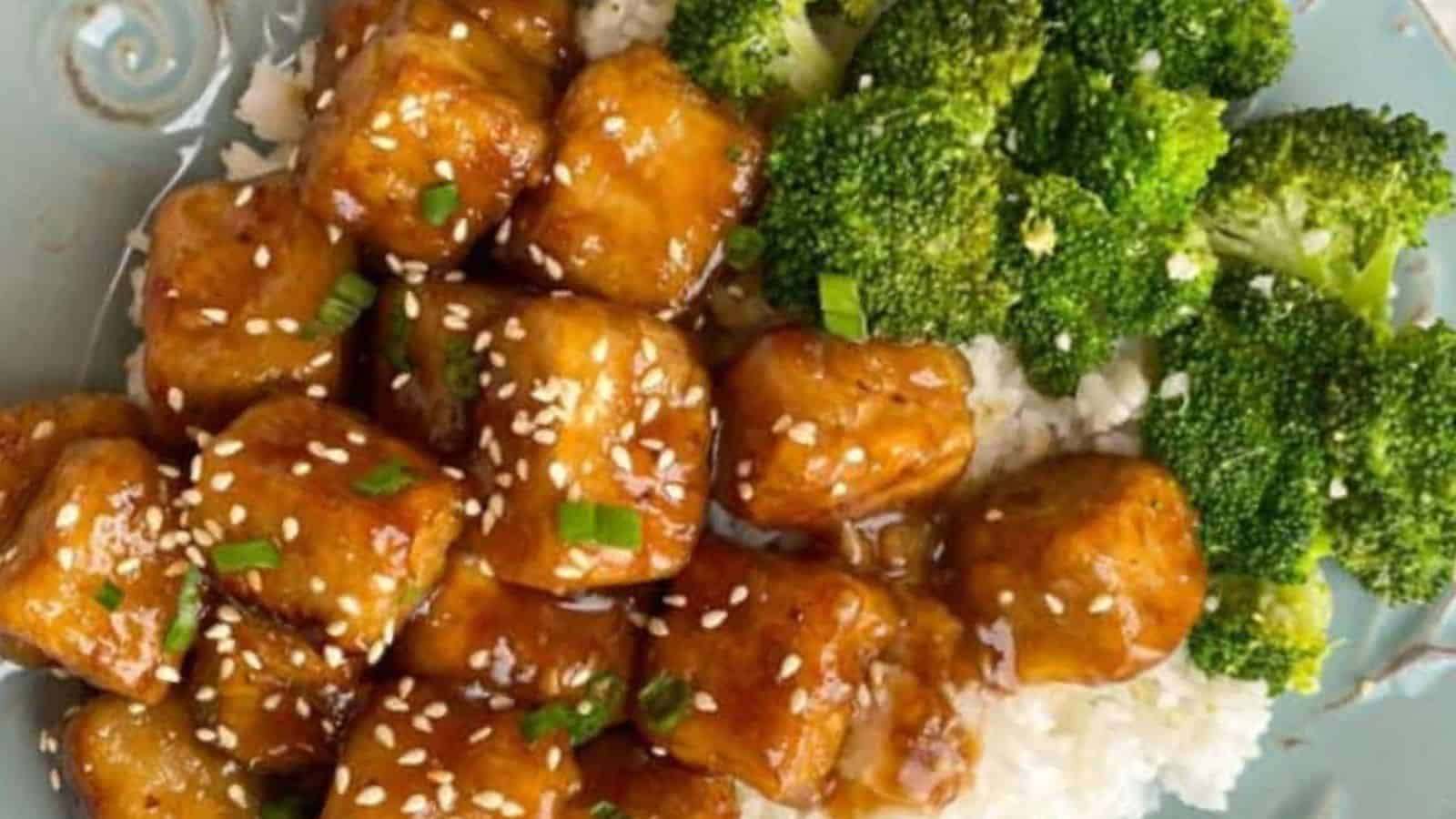 Glazed tofu cubes with sesame seeds and chives on rice, accompanied by steamed broccoli.