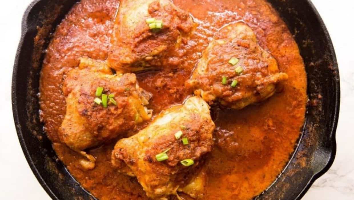Cast Iron Chicken Thigh in Creamy Tomato Sauce with a spoon in a cast iron skillet.